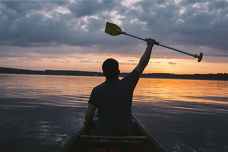 man riding boat raising his paddle photo thumbnail