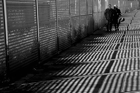 man and woman walking beside fence grayscale photography thumbnail