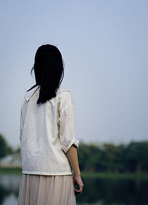 woman in white dress shirt facing body of water thumbnail