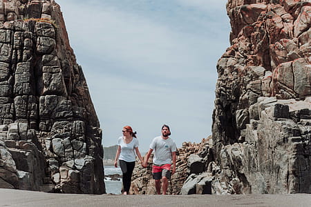 Woman and Man Holding Hands While Walking Between Rock Formation thumbnail