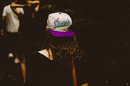 woman in black top wearing purple and white cap against black background thumbnail