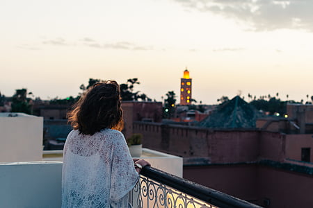 woman in white floral top holding black metal railing overlooking buildings thumbnail