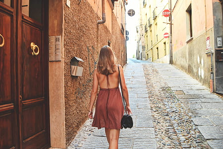 woman wearing brown backless dress walking near brown concrete building during daytime thumbnail
