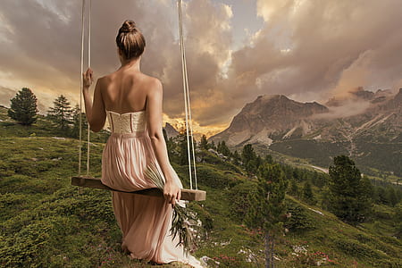 woman in maxi dress sitting on swing facing mountains thumbnail