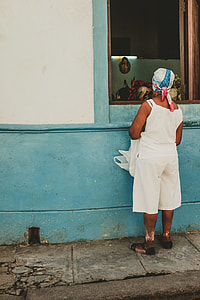 woman wearing white camisole standing in front of petaled flowers on window thumbnail