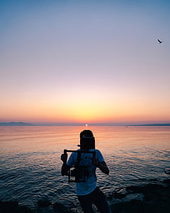 man holding camera stabilizer on seashore during sunset thumbnail