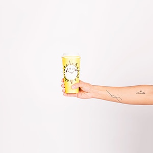 person with tattoos holding yellow disposable cup thumbnail