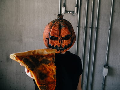 person with pumpkin mask holding pizza slice thumbnail
