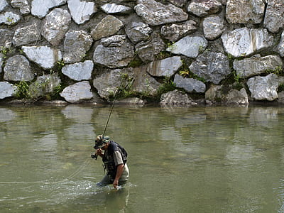 man standing on body of water while holding fishing rod thumbnail
