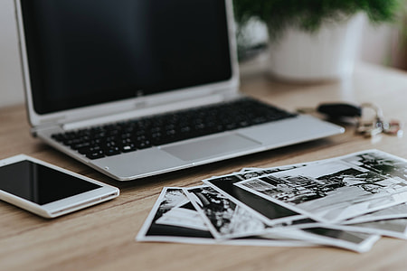 Black-and-white photos with a silver laptop, a smartphone, car keys, pencils and a camera thumbnail
