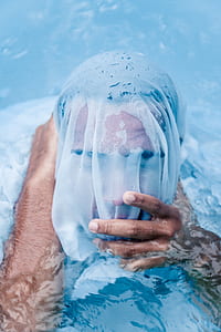 man covering face by white plastic pack on body of water thumbnail
