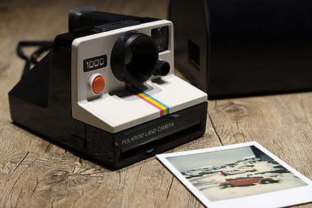 white and black Polaroid 1000 land camera beside red vehicle photo on brown wooden table thumbnail
