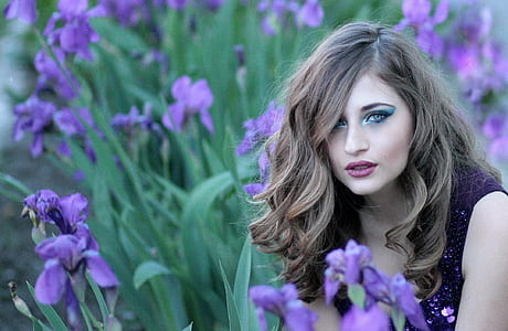 selective focus photo of woman in purple top sitting beside purple flowers thumbnail