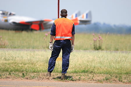 man wearing orange high-visibility vest standing near green grass during day thumbnail