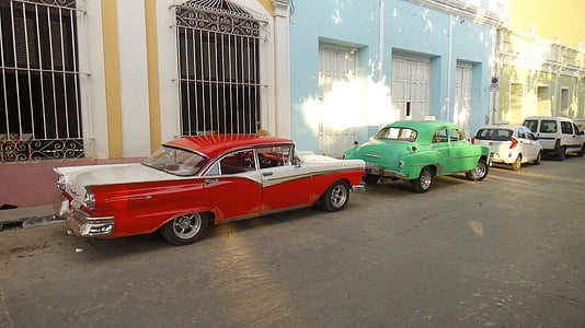 two red and green sedan park beside blue and gray painted buildings thumbnail