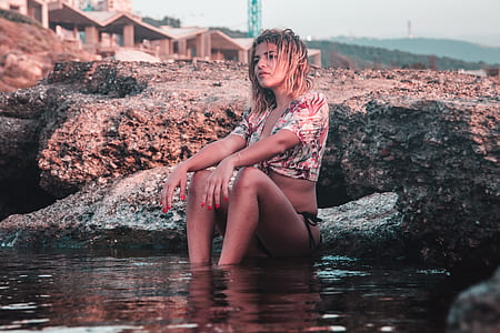 woman wearing crop top and bikini bottoms sitting beneath body of water thumbnail