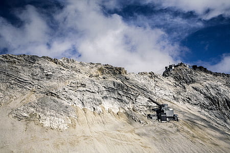 building beside rocky mountain under cloudy sky thumbnail