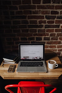 Creatives desk with laptop, camera, journals and books in front of brick wall thumbnail