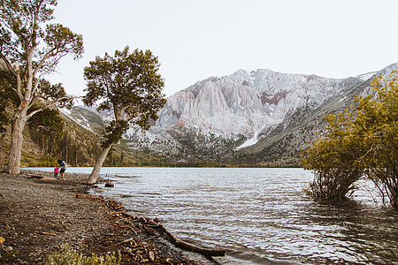 view of snow covered mountain top from across body of water with two persons at shore thumbnail