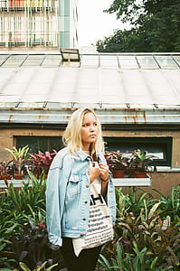 Woman Wearing White Shirt and Denim Jacket Standing Near House thumbnail