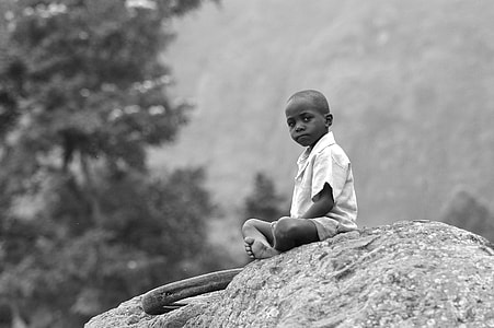 grayscale photography of boy sitting on rock outdoor thumbnail