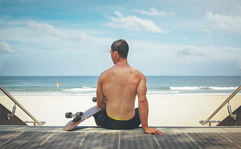 man sitting on staircase holding brown cruiser board near beach during daytime thumbnail