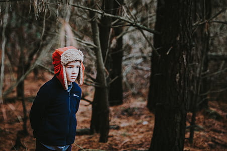 boy with black jacket and red hat waling in the middle of forest thumbnail
