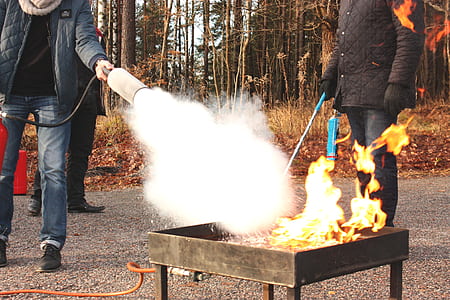 person firing out the fire using fire extinguisher standing beside man holding stick during daytime thumbnail
