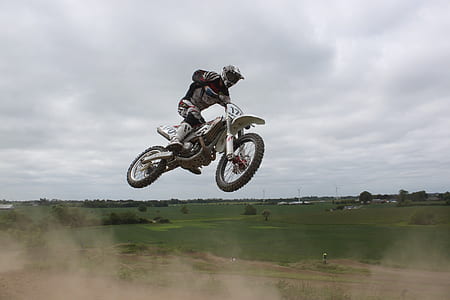 Man Riding Moto Cross Bike Doing Tricks Mid Air Under Cloudy Skies during Daytime thumbnail