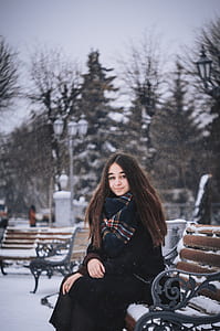 woman wearing black coat sitting on black and brown bench thumbnail