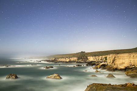 brown concrete cliff near body of water under blue sky thumbnail