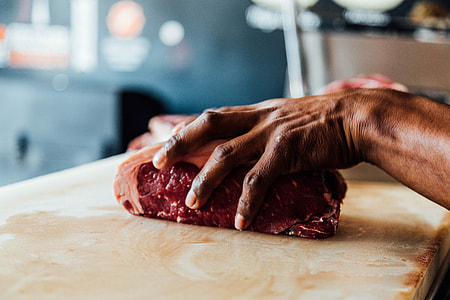 selective focus photography of person holding piece of meat placed on beige wooden board thumbnail