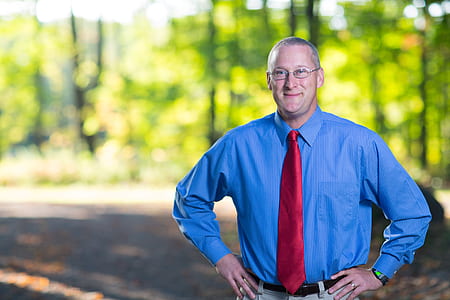 smiling man wearing blue striped dress shirt and red necktie outdoors thumbnail