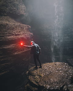 man holding red light inside cave beside waterfall thumbnail