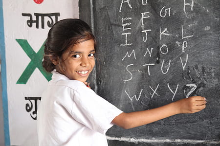 girl holding chalk while writing alphabet on board thumbnail