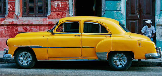 classic yellow sedan parked near blue and red painted concrete structures thumbnail