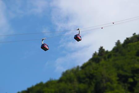 two red cables cars over green trees at daytime thumbnail