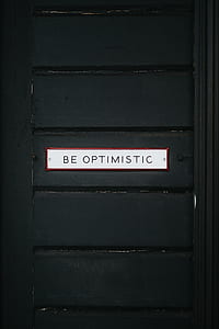 black wooden door with white Be Optimistic signage thumbnail