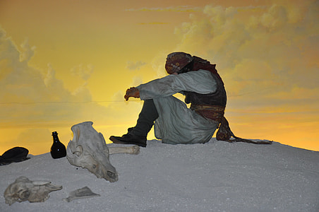 man sitting on hill beside animal skull thumbnail