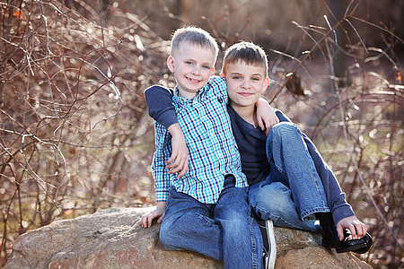 boy's in long sleeve shirt next to a boy in blue and black button up shirt sitting on rock thumbnail