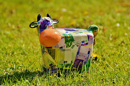 blue and multicolored euro banknote-themed cow coin bank on green grass thumbnail