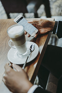 man holding iPhone beside coffee latte thumbnail