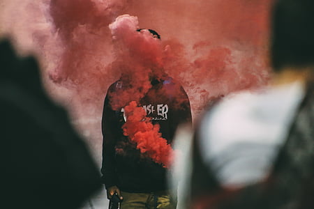 person wearing black Trasher shirt covered with pink smoke at daytime thumbnail