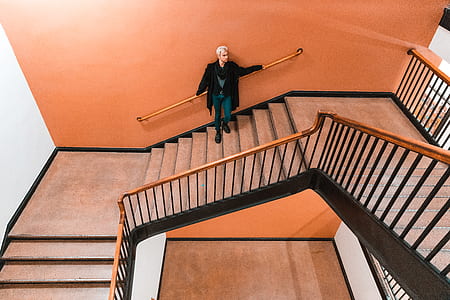 person standing and leaning on orange painted wall holding brown handrail on stairway thumbnail