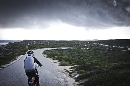 person riding bicycle on black road under cloudy sky during daytime thumbnail