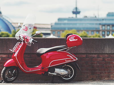 red motor scooter parked beside brown wall thumbnail