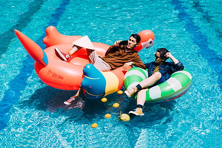 two men riding red flamingo and green and white striped inflatable ride thumbnail