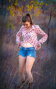 woman wearing pink dress shirt and blue denim cut-off shorts standing on grass during daytime thumbnail