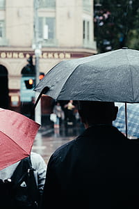 man holding black umbrella standing near the building thumbnail