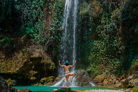topless man standing near waterfall thumbnail
